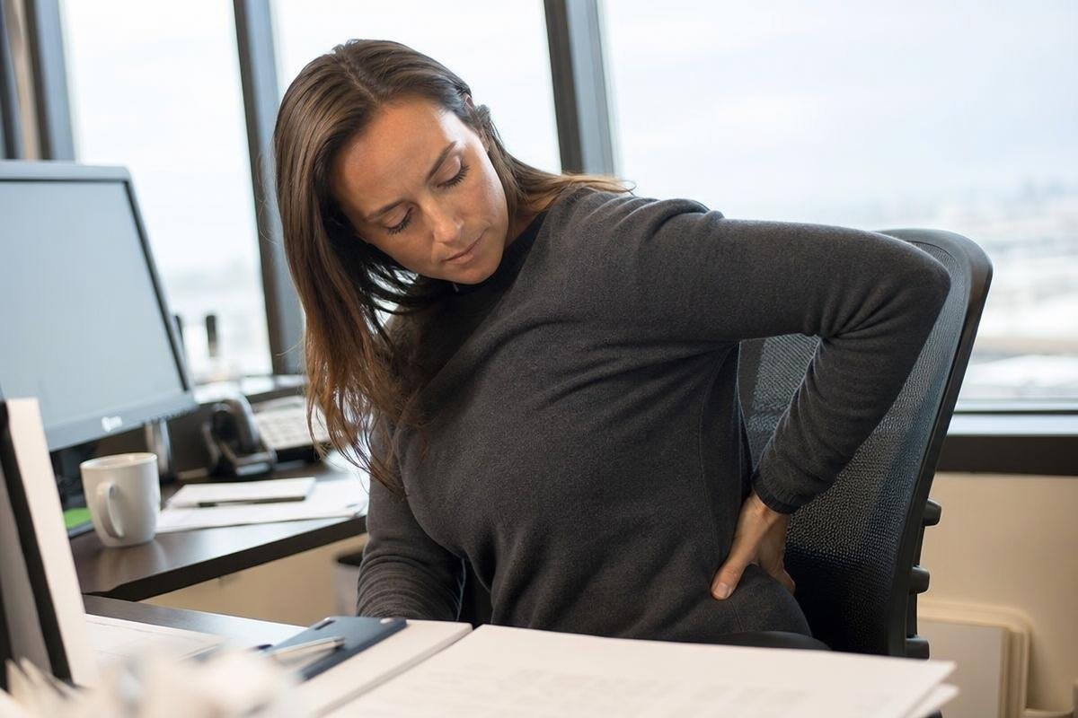 Woman sitting at a desk holding her lower back in pain