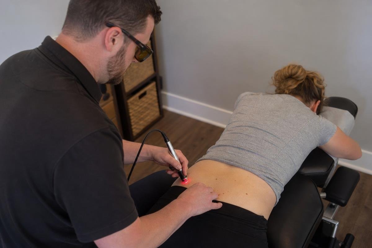 A chiropractor performing cold laser therapy on a patient's lower back